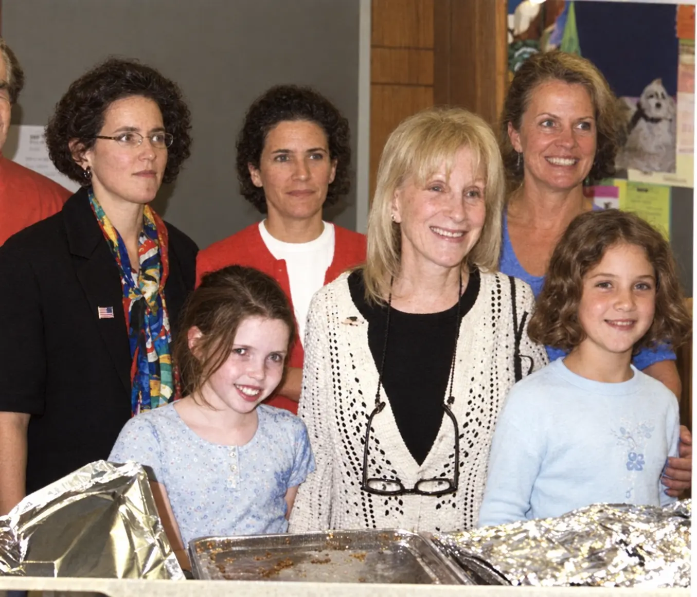 Adults and children stand behind trays of prepared food.