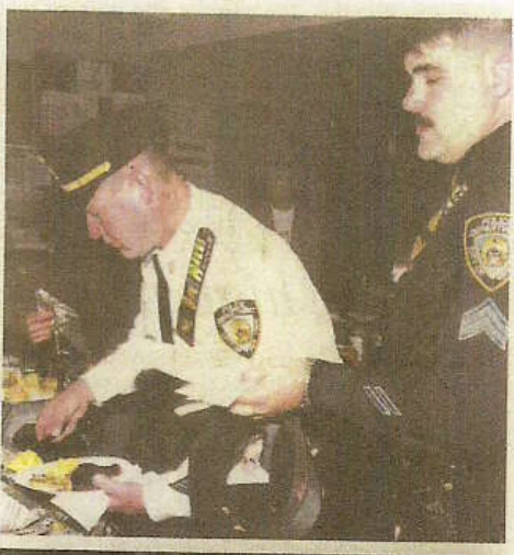 Two uniformed officers hold plates while serving themselves at a food table.